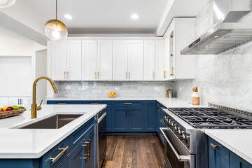 A luxurious white and blue kitchen with gold hardware, stainless steel appliances, and white...