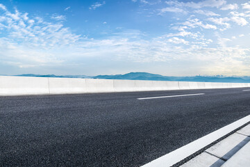 Empty asphalt road and mountains with city skyline