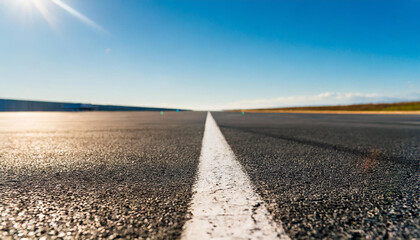 Surface level of long airport runway with directional marking against clear sky on sunny day..