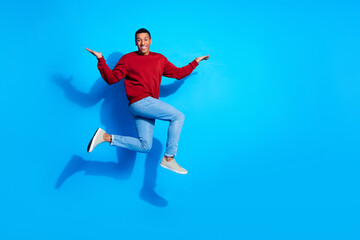 Fototapeta premium Full size profile photo of sporty carefree person jump run arms hold empty space isolated on blue color background