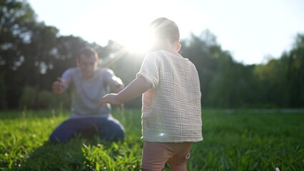 baby takes first steps in the park. happy family kid dream concept. dad teaches his son to walk takes the first steps lifestyle in the park on green grass. baby son taking first steps