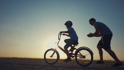 family play in the park. father teaching son to ride a bike. happy family kid dream concept. son...