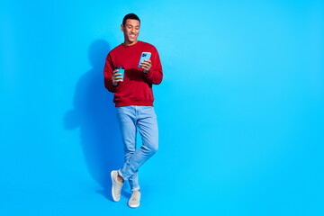Fototapeta na wymiar Full size photo of cheerful person hold coffee cup chatting smart phone empty space isolated on blue color background