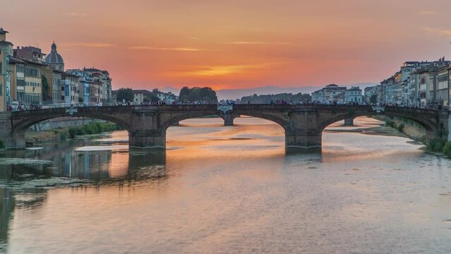 Cityscape viewfrom above on Arno river with famous Holy Trinity bridge timelapse on the sunset in Florence. Reflections on water. Orange sky
