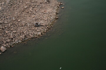 Environmental Degradation: Pollution in Tranquil Waters.  juxtaposition of a lake with a littered pebbly shore, highlighting environmental challenges.