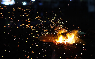 Burning flames and sparks are visible on a dark background with a fire at night.