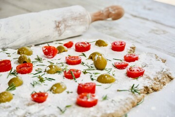 Preparing a focaccia with cherry tomatoes and olives and rosemary leaves.