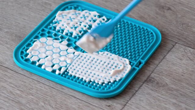 snack mat, licking mat for cats and dogs. hand putting yogurt to dog lick mat