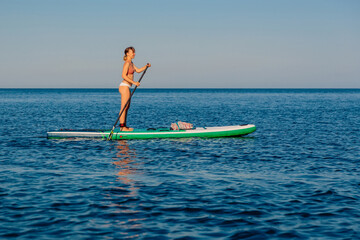 Woman paddling on stand up paddle board, sea on sunny summer day. Relaxing on blue ocean