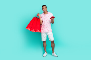 Full size photo of handsome guy dressed casual print t-shirt shorts holding new outfit smartphone isolated on teal color background