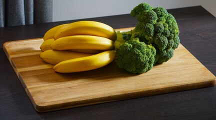 Dojrzałe banany i brokuł gotowy do pokrojenia. Świeże owoce i warzywa na stolnicy. Stół, deska do krojenia, banany i brokuł - obrazy, fototapety, plakaty