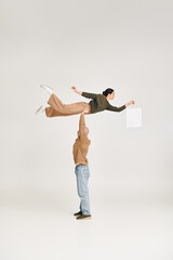 strong man in casual attire lifting woman with shopping bag, balancing in a playful pose in studio