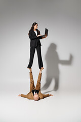 Woman in business attire with laptop balancing on feet of man formal wear, couple of acrobats - 753015548