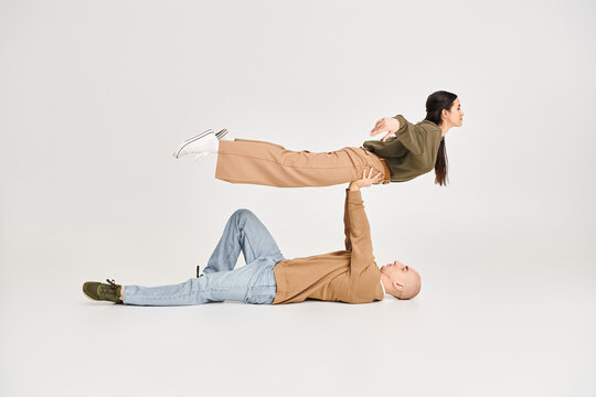 strong man in casual wear lying on floor and lifting brunette woman in studio, couple of acrobats