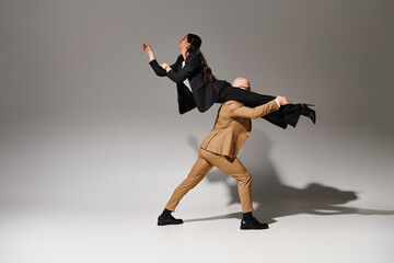Fototapeta na wymiar man in formal attire lifting brunette and graceful woman in suit balancing during dance in studio