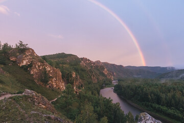 A mountain rock landscape at sunset with a rainbow in summer. The river is at the foot of the rocky hills. Shaman's Trail, Khakassia, Russia