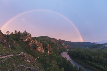 A mountain rock landscape at sunset with a rainbow in summer. The river is at the foot of the rocky...