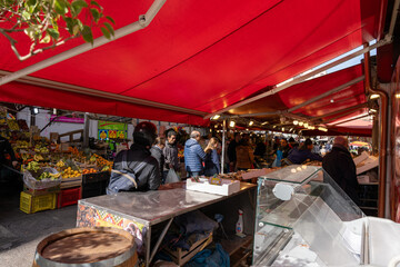 A group of people are shopping at a market with a red canopy