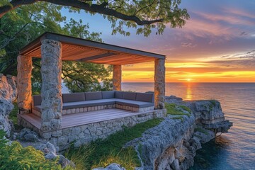 A stone covered gazebo overlooking the ocean with a sunset in the background