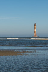 Morris Island Lighthouse from the shoreline of Folly Beach near Charleston, South Carolina. - obrazy, fototapety, plakaty
