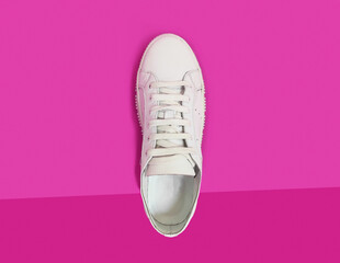 White sports sneakers with laces on a pink background