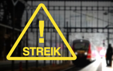 Bahnstreik, gelbes Warndreieck mit Ausrufezeichen und Streik Schriftzug, im Hintergrund ein Bahnhof...