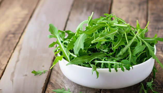 Fresh green arugula leaves on white bowl, rucola rocket salad on wooden rustic background with place for text. Selective focus, healthy food, diet. Nutrition concept. selective focus, bokeh, copy spac