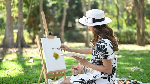 Slow motion shot of beautiful young woman painting a picture in the park. Mindfulness, art therapy and creative hobbies concept