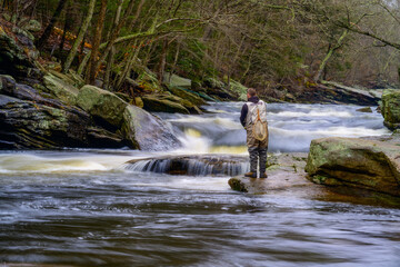 Photograph of a man fishing from a rock in the middle of rapids