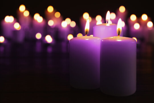 Burning violet candles in darkness, space for text. Funeral attributes