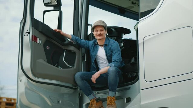 Portrait of happy truck driver man sitting in the cab and looking at the camera