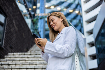 Cropped shot of a Young female doctor using her smartphone while standing. Female nurse surfs net...