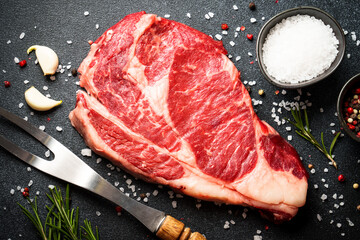 Meat steak. Beef steak ribeye with spices and herbs on black background. Flat lay close-up..