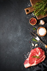 Raw meat steak with spices on black background. Beef steak ribeye. Top view with copy space.