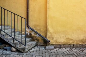 Fragment of the wall of a yellow plastered building. There is a drainpipe and a concrete staircase with handrails. Background.