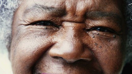 Obraz premium One happy black senior woman tight macro close-up of eyes and face looking at camera smiling. Wrinkled African American person in 80s showing wisdom and old age