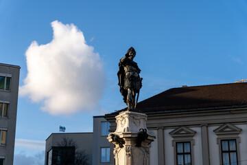 The statue is surrounded by a white pedestal, and the building has a brown roof