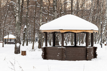 wooden gazebo with a snow-covered roof in a winter park