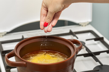 woman's hand salts water in a pan.