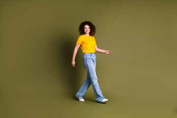 Full length body photo of young cheerful student woman in yellow t shirt and jeans walking alone isolated on khaki color background