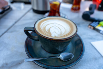 A cup of coffee with a white swirl on top sits on a blue saucer
