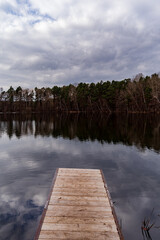 A Wooden Dock Overlooking a Calm Lake Surrounded by Forest Under a Cloudy Sky