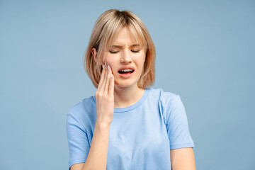 Sad upset young woman touching cheek, having toothache isolated on blue background