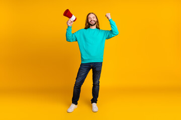 Full size photo of attractive guy hold loudspeaker raise fist achievement empty space isolated on yellow color background