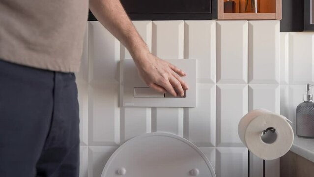 Concerned about water conservation, the man pressing button the eco-friendly toilet for low-flow flush. The economical flushing mechanism helps maintain a clean and hygienic restroom environment.
