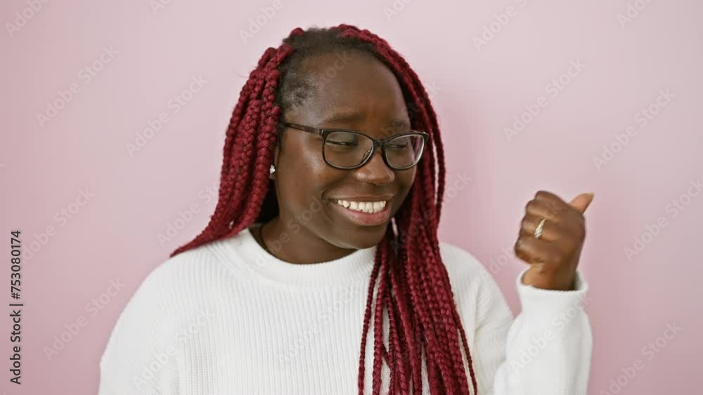 Sticker portrait of a cheerful black woman with braids pointing thumb over pink background.