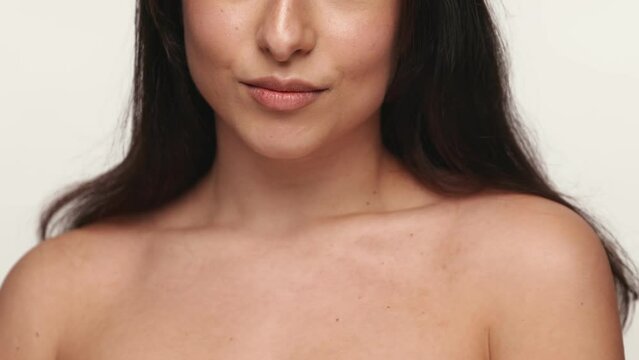 An enchanting woman with a bare shoulders bites her lip and kissing gesture, provocatively, creating desire and sensuality on a white backdrop