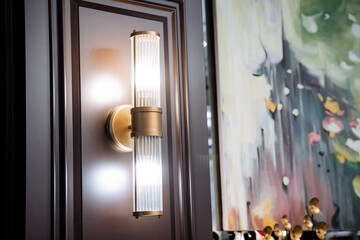 A wall light fixture hangs near a painting on the hardwood wall of a building
