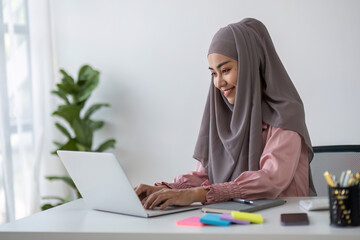 Smiling Muslim business woman Wearing a hijab while chatting online on a work desk in the office.