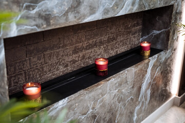 Three candles on a shelf in a fireplace inside a brick house